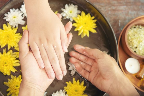 Female hands and bowl of spa water with flowers, close up. Hands